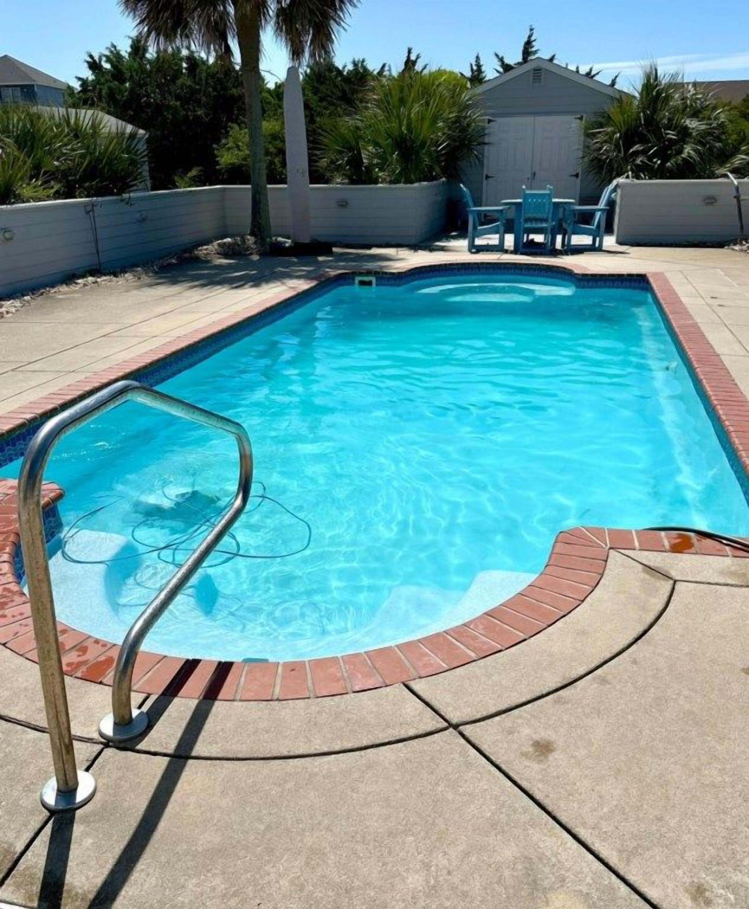 Ein rechteckiger Pool mit Metallschutzrail, umgeben von einer Ziegelumrandung und einer Betonplattform.