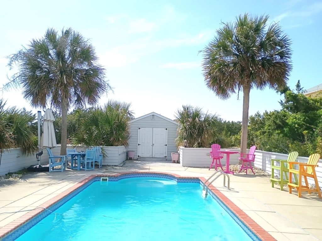 A swimming pool with a tiled edge, surrounded by palm trees, and outdoor furniture.