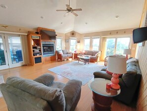 A spacious living room with a fireplace, multiple seating areas, and a ceiling fan.