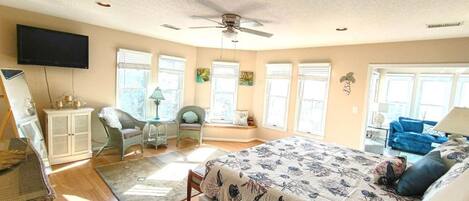 A bedroom with a bed, a television, a ceiling fan, and a window with blinds.