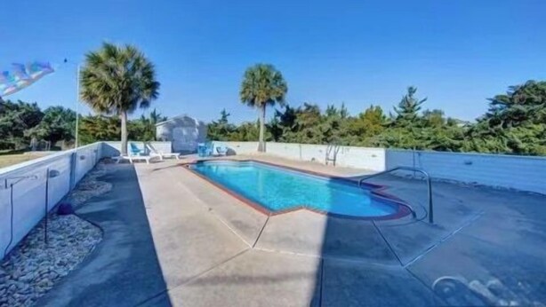 A swimming pool with a clear blue water, surrounded by a concrete deck, palm trees, and a clear sky. - Oceanview/Elevator/Pool/Hot tub/Steps to beach (Rodanthe)
