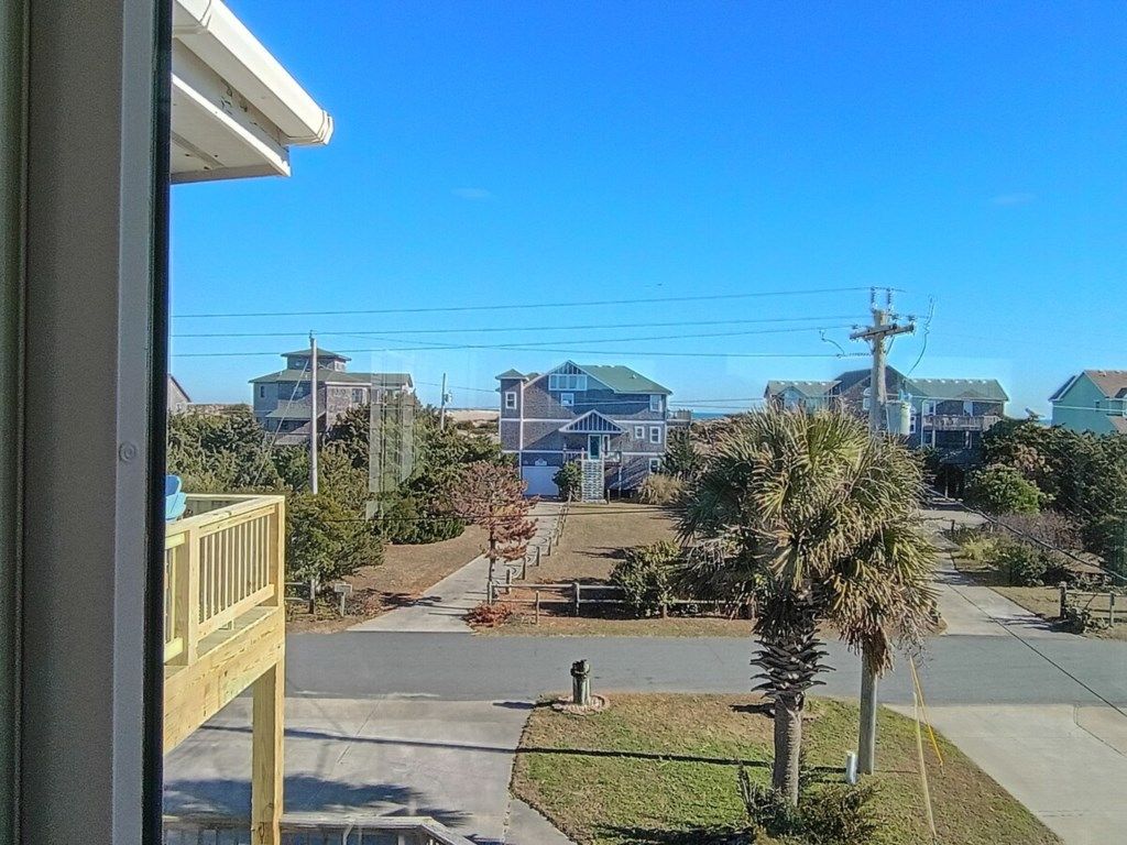 Una calle residencial con casas, cielo despejado y una palmera.
