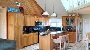 Una cocina con armarios de madera, una isla central con taburetes de bar, un microondas y un refrigerador.