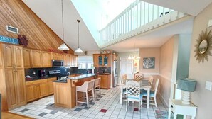 A kitchen with wooden cabinets, a central island, and a dining area with a table and chairs. - Oceanview/Elevator/Pool/Hot tub/Steps to beach (Rodanthe)