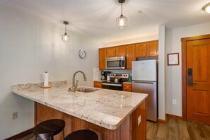 Une cuisine dotée de plans de travail en granit, d’armoires en bois, d’appareils électroménagers en acier inoxydable et de luminaires suspendus.
