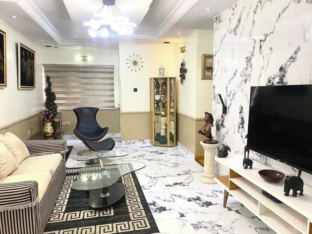 A modern living room with a sofa, a glass coffee table, a TV on a stand, and a decorative wall with a clock and a statue.