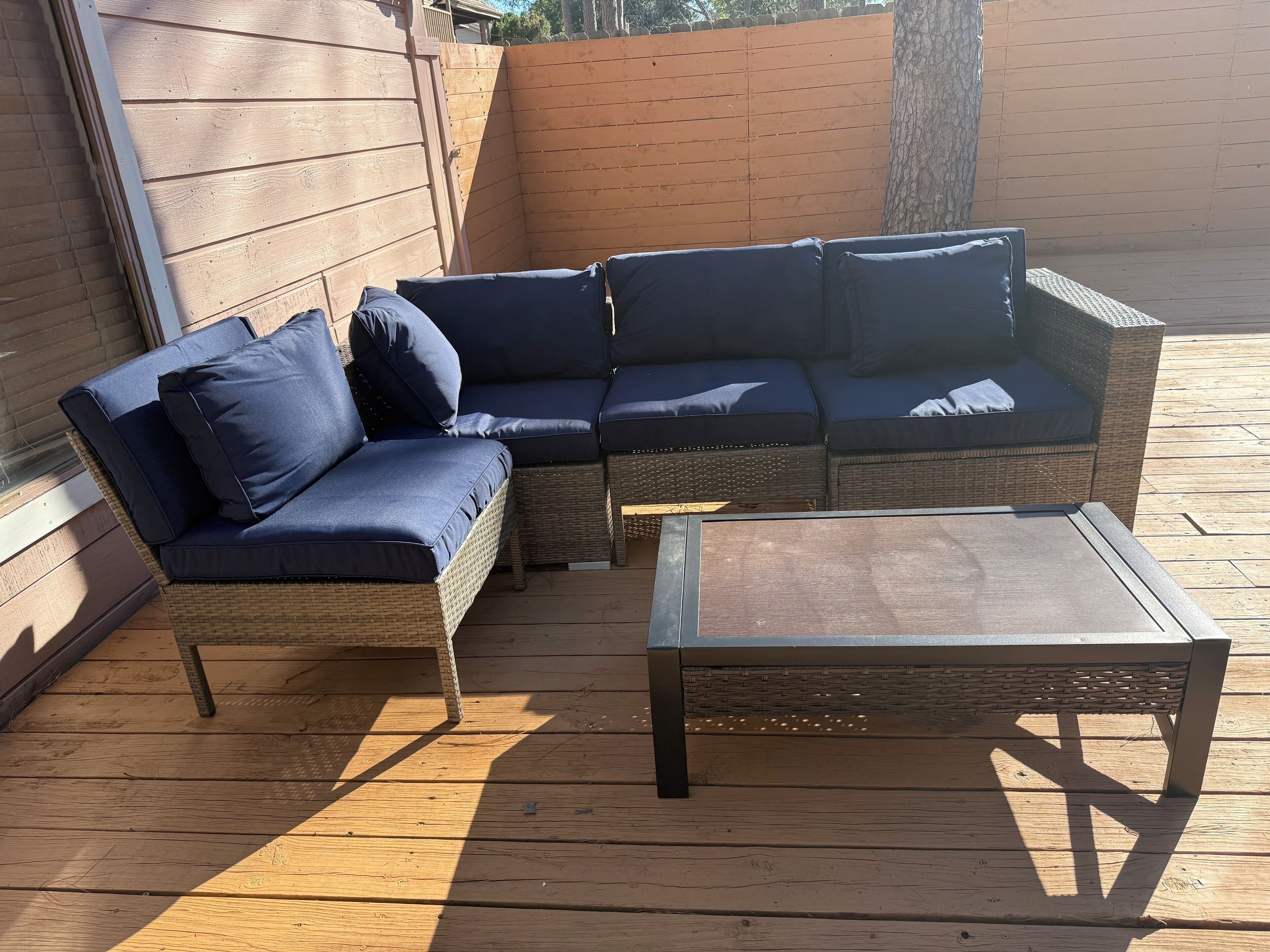 A wooden deck with a wicker sofa and a metal coffee table.