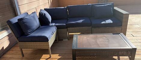 A wooden deck with a wicker sofa and a metal coffee table.