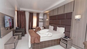 A modern hotel room with a large bed, a bedside table, a desk, and a chair. - HOUSE 36 (Lagos)
