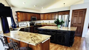 A spacious kitchen with wooden cabinets, granite countertops, and a central island with bar stools. - The Grove. Blackfoot. Spacious 4BR. Sleeps 16+  Retreat By Yellowstone (Blackfoot)