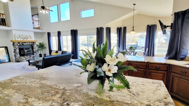 A spacious living room with a stone fireplace, a modern kitchen with granite countertops, and large windows offering views of the outdoors. - The Grove. Blackfoot. Spacious 4BR. Sleeps 16+  Retreat By Yellowstone (Blackfoot)