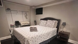 Une chambre à coucher comprenant un lit, des tables de chevet, un téléviseur fixé au mur et un porte-manteau.