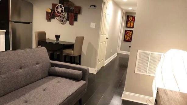 Un salon moderne avec un canapé gris, une table à manger avec des chaises et un coin cuisine équipé d’un réfrigérateur.