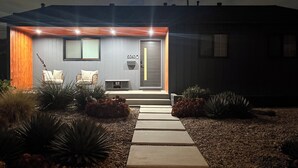 Una casa moderna con un porche delantero, una puerta con número y un pequeño espacio de descanso con una silla y un banco.