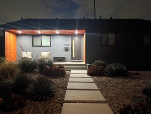 Ein modernes Haus mit Veranda, einer Tür mit Hausnummer und einer kleinen Sitzgelegenheit mit Stuhl und Bank.