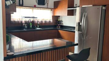 Une cuisine moderne avec des meubles en bois, un réfrigérateur en acier inoxydable, un coin bar avec des tabourets et un ventilateur de plafond.