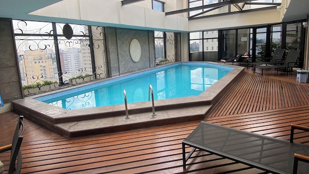 A rooftop pool area with a glass balustrade, wooden deck, and lounge chairs. - Comfortable and fully equipped apartment in the heart of Jardins. (São Paulo)