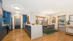 Moderni keittiö, jossa on keskeinen keittiösaareke, puulattia ja integroidut kodinkoneet.
