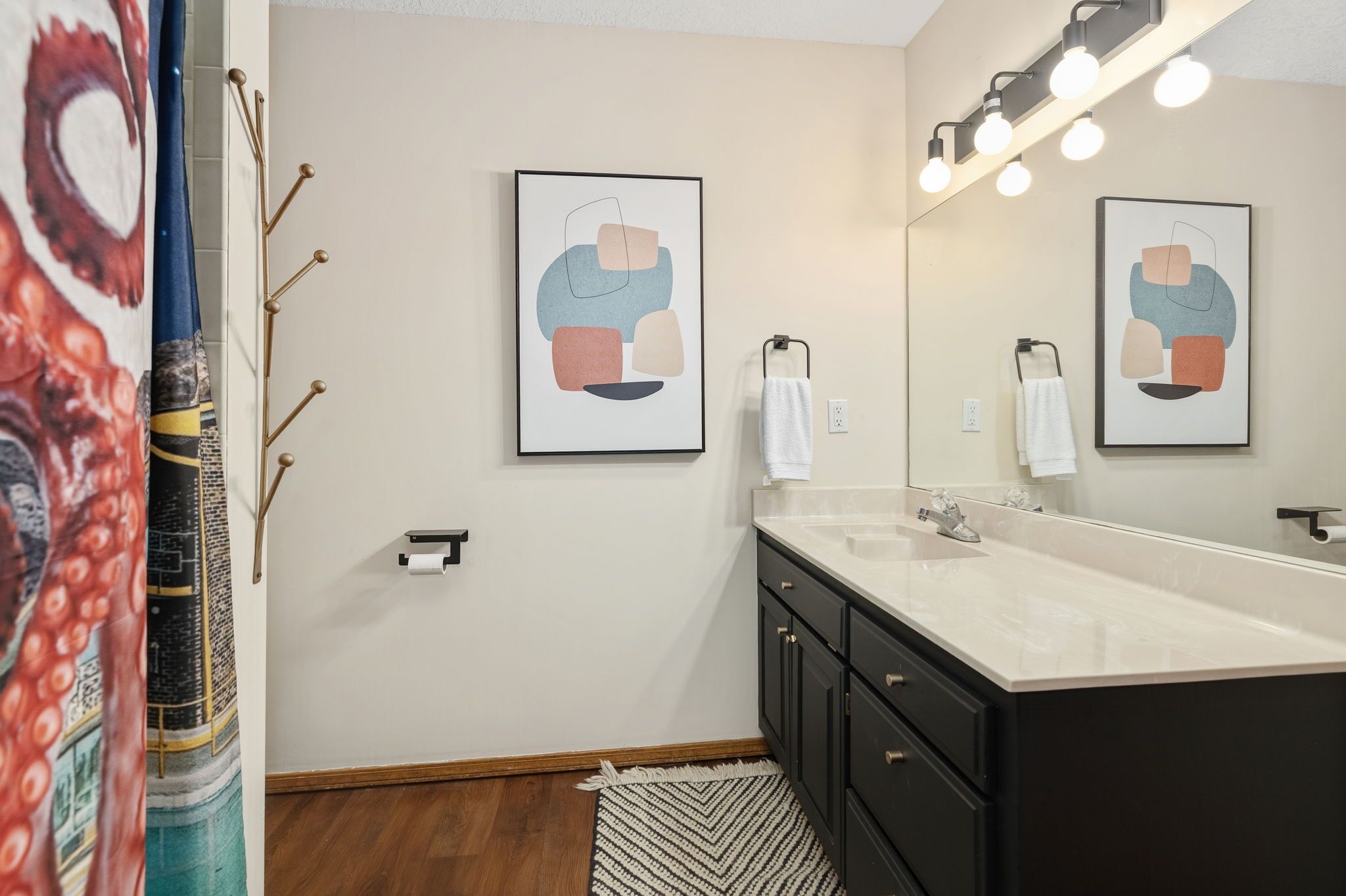 A modern bathroom with a large mirror, two framed abstract art pieces, a white sink, and black cabinets.
