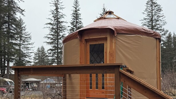 A wooden yurt with a deck and a ramp, surrounded by trees. - Salmon Spot (Seward)