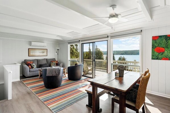 A spacious living area with a gray sofa, black chairs, a wooden dining table, and a colorful striped rug.