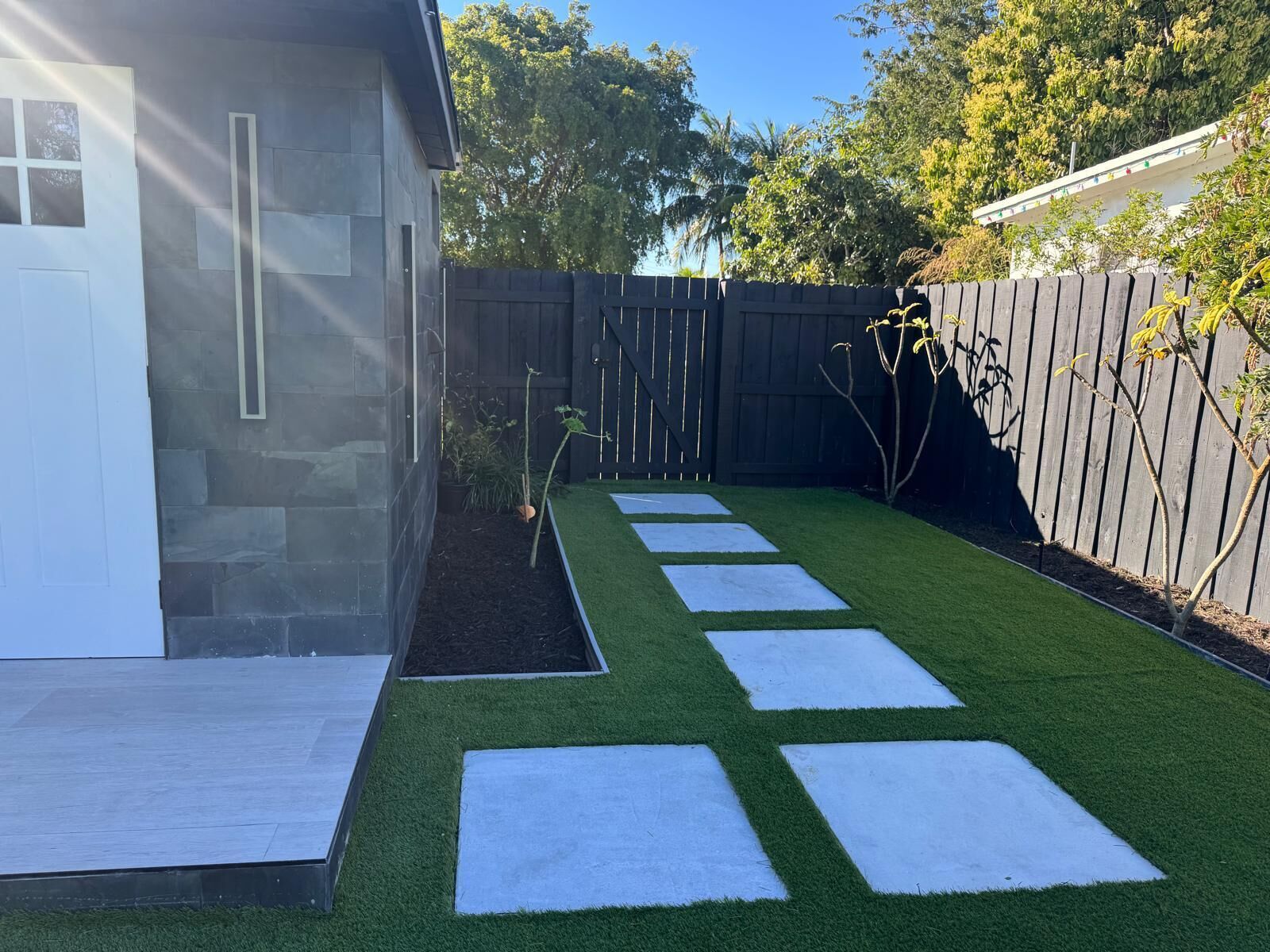 Een achtertuin met kunstgras, een houten terras en een houten omheining.