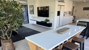 A modern kitchen with a central island, bar stools, a large potted plant, and a flat-screen TV mounted above the island. - Newly renovated top to bottom Beautiful 2-bedroom house (Pompano Beach)