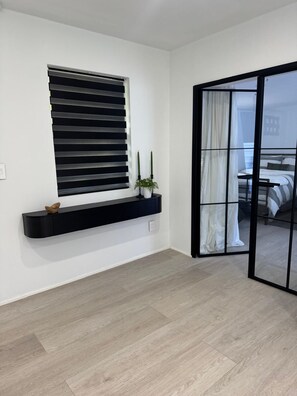 Ein modernes Zimmer mit einem schwarzen Fensterrahmen, einer schwarzen, schwebenden Ablage mit Dekoration und Blick durch eine Glastür in einen anderen Raum.