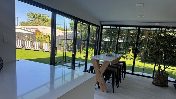 A modern kitchen with large windows, a white countertop, and a dining area with stools. - Newly renovated top to bottom Beautiful 2-bedroom house (Pompano Beach)