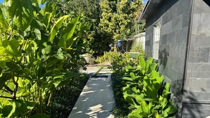 A pathway flanked by lush greenery and a stone building. - Newly renovated top to bottom Beautiful 2-bedroom house (Pompano Beach)
