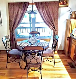 A dining area with a round table, four chairs, and a view of a balcony. - Charming Lakeside Cabin on Lookout mountain, Fort Payne by Little River Canyon! (Fort Payne)