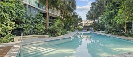 A swimming pool surrounded by lush greenery and modern buildings.