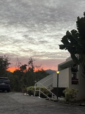 A modern building with a staircase leading to a balcony, surrounded by greenery and a sunset in the background. - Book a getaway by 9/30/26 for 11/2026 and Receive a gift upon check-in! (St Thomas, USVI)