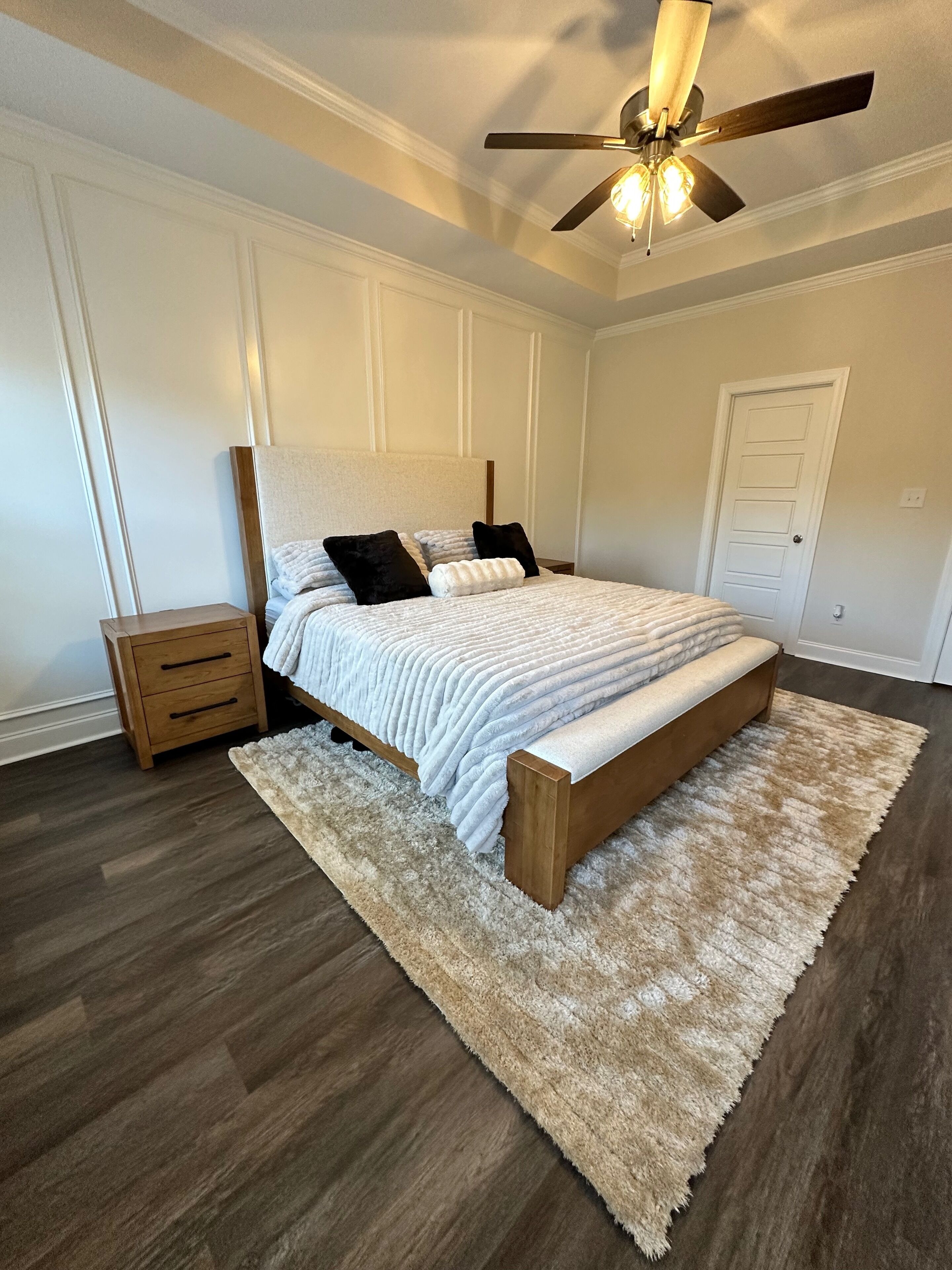 Une chambre à coucher avec un lit, une table de chevet en bois et un ventilateur de plafond.