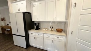 Una cucina moderna con mobili bianchi, un frigorifero nero, una macchina da caffè e una ciotola di legno sul piano di lavoro.