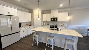 Una cucina moderna con mobili bianchi, una grande isola con sgabelli, elettrodomestici in acciaio inossidabile e illuminazione a sospensione.