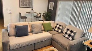Een woonkamer met een hoekbank, een bijzettafeltje en een potplant.