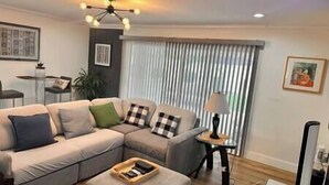 Een woonkamer met een hoekbank, een bijzettafeltje, een lamp en een plafondarmatuur.