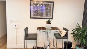 Een klein zithoekje met een glazen tafel, twee stoelen, een lijstwerk aan de muur en een potplant.