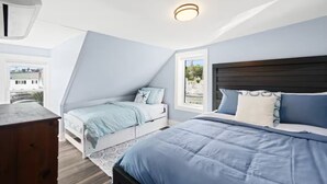 Ein Schlafzimmer mit schrägem Dach, einem großen Bett, einem kleineren Bett und einer Holzkommode.
