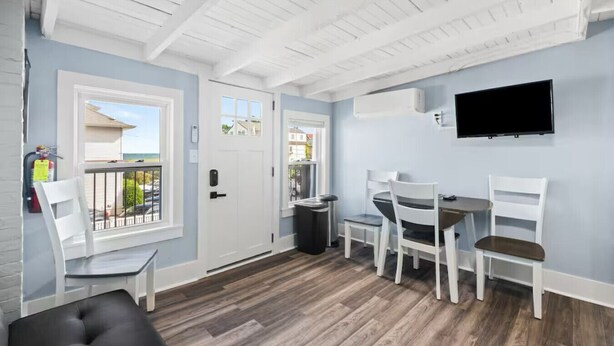 Ein Zimmer mit Balkon, einem Essbereich mit Stühlen und Tisch, einem flachbildfernseher an der Wand und einem Feuerlöscher an der Wand.