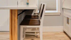 A kitchen with a wooden beam ceiling, a white countertop, a dark wooden chair, and a window with blinds. - Charming Beachfront Loft | New Renovation (Old Orchard Beach)