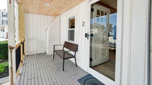 A covered outdoor area with a wooden ceiling, a bench, and a glass door leading to a covered patio. - Charming Beachfront Loft | New Renovation (Old Orchard Beach)
