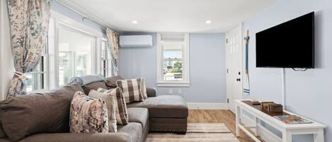 A modern living room with a sofa, a TV, and a window with curtains.