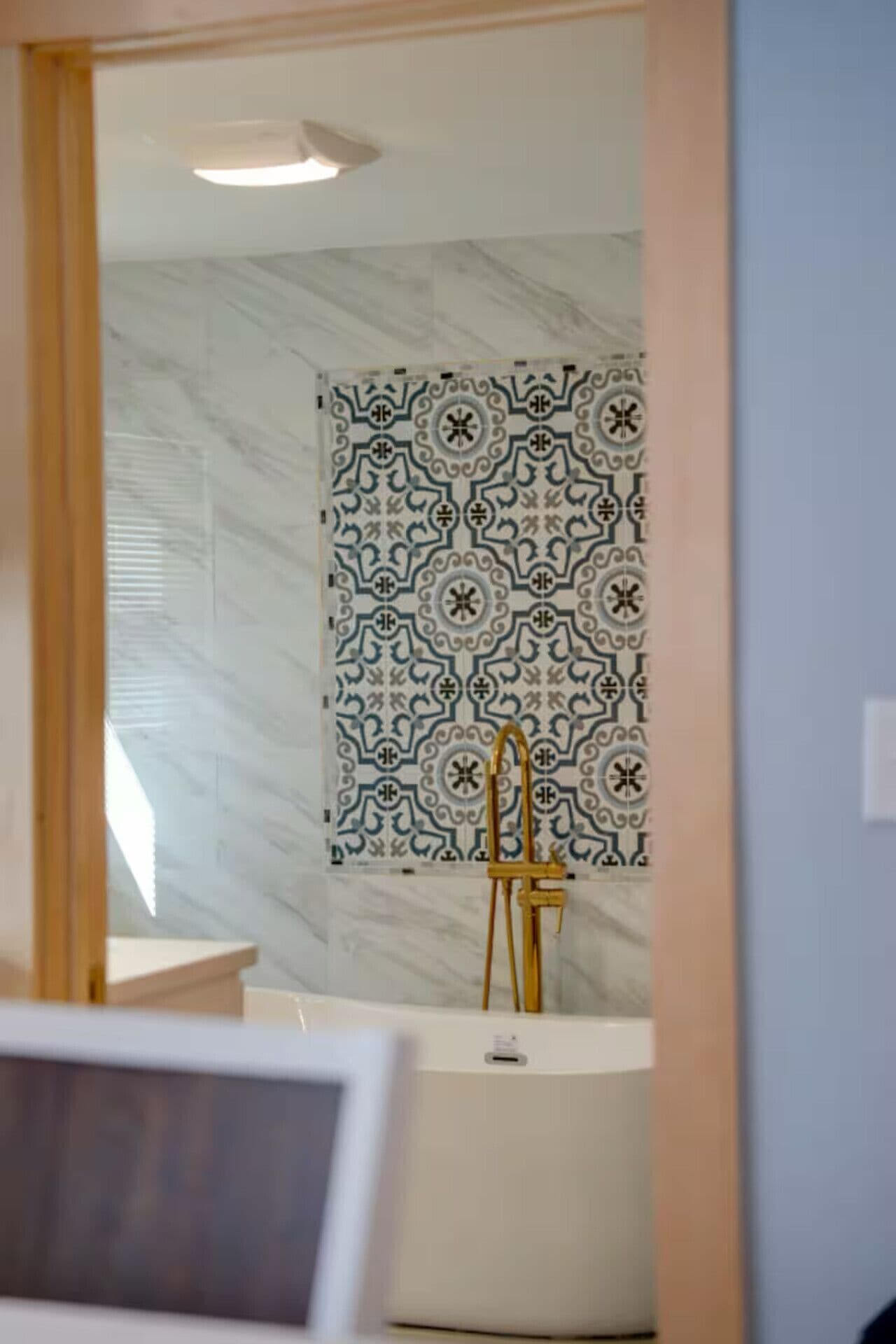 A bathroom with a white bathtub, a gold faucet, and a patterned tile wall.