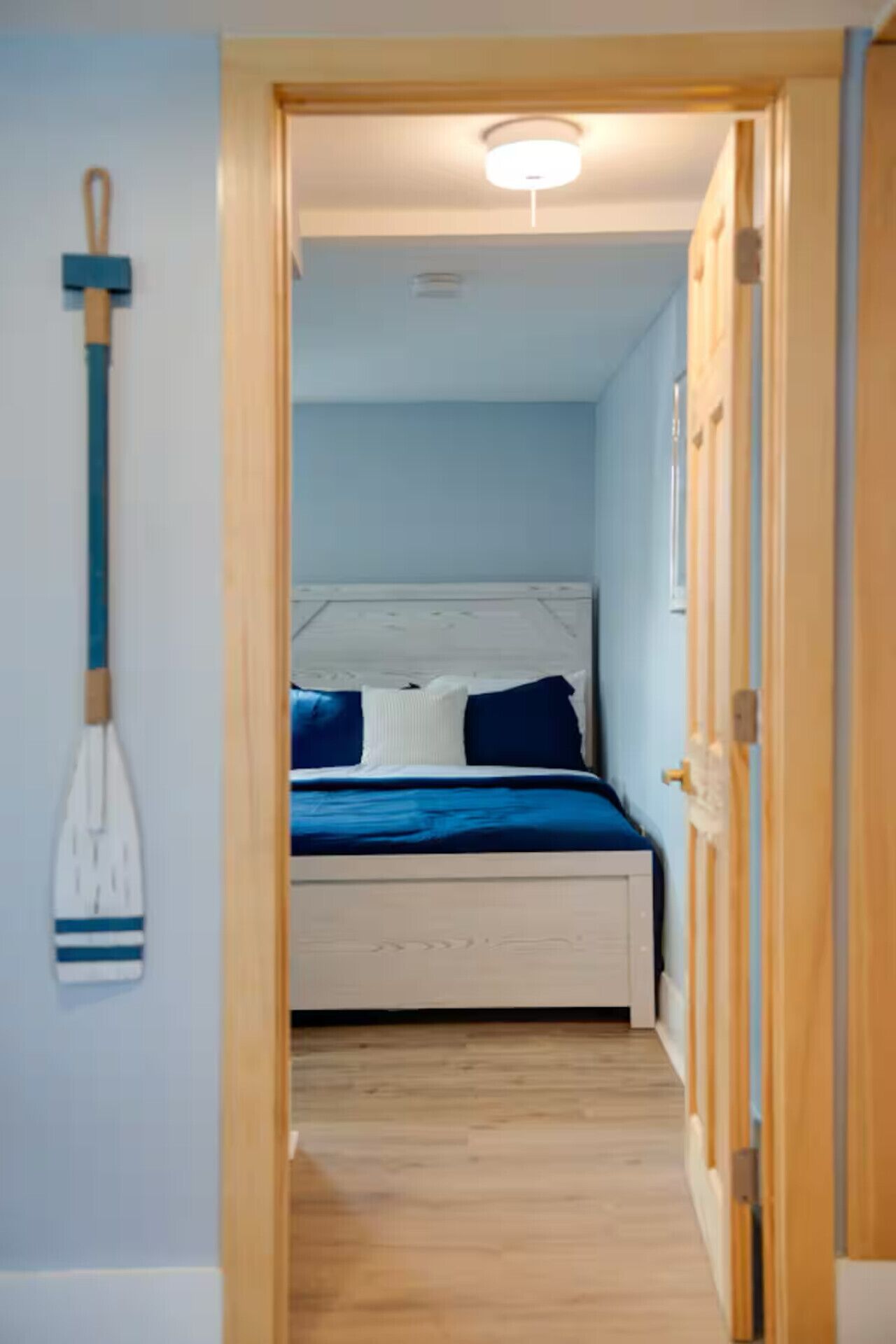 A narrow hallway leading to a bedroom with a bed, a ceiling light, and a mop leaning against the wall.