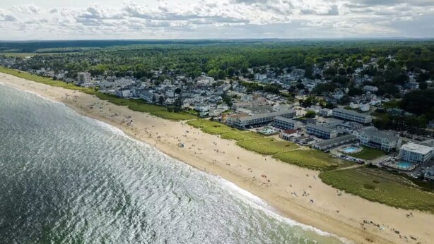 Eine Luftaufnahme einer Küstenstadt mit sandigem Strand, Strandhäusern und einem dicht besiedelten Wohngebiet.