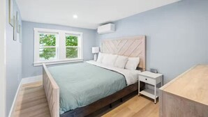 Ein Schlafzimmer mit Bett, Nachttischen, einem Fenster mit Blick auf Grünflächen und einer hellblauen Wand.