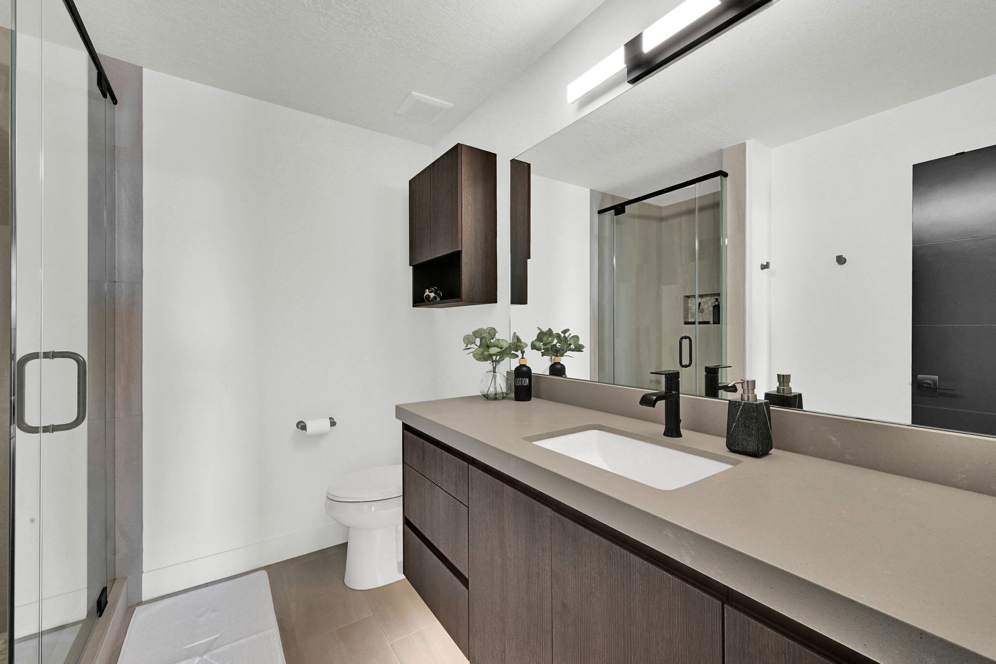 A modern bathroom with a large mirror, a double sink, and a glass shower enclosure.