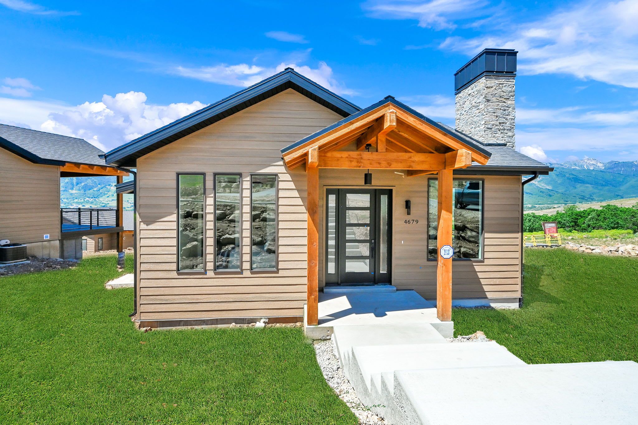 Une maison moderne avec une façade en bois, une cheminée en pierre et une vue dégagée sur le paysage environnant.